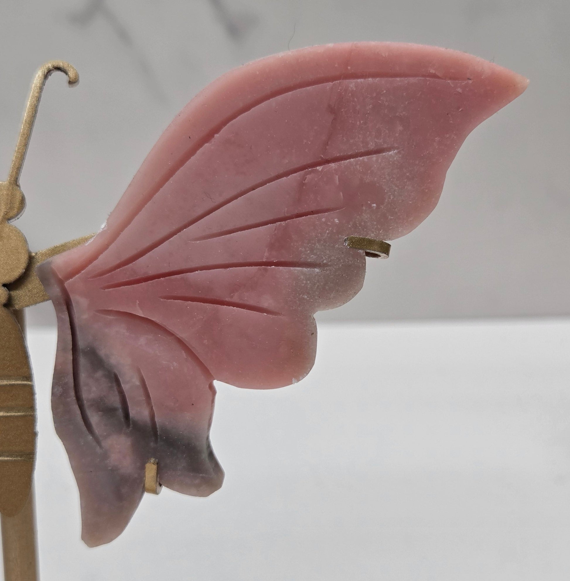 Pink Opal crystal wing carvings on a gold metal stand on a white background