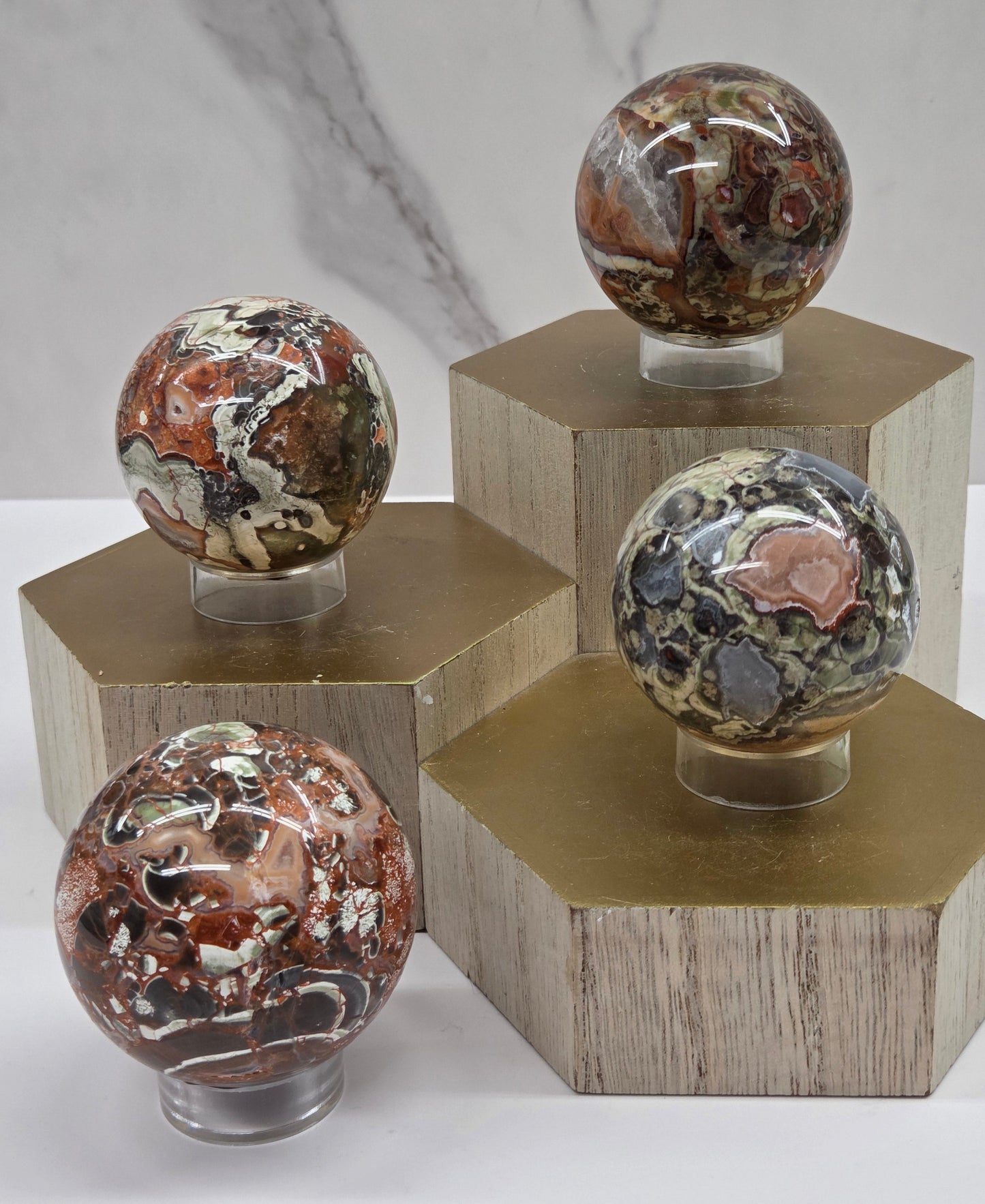 Decorative money agate spheres with multiple colors and patterns on a wooden stand against a white background