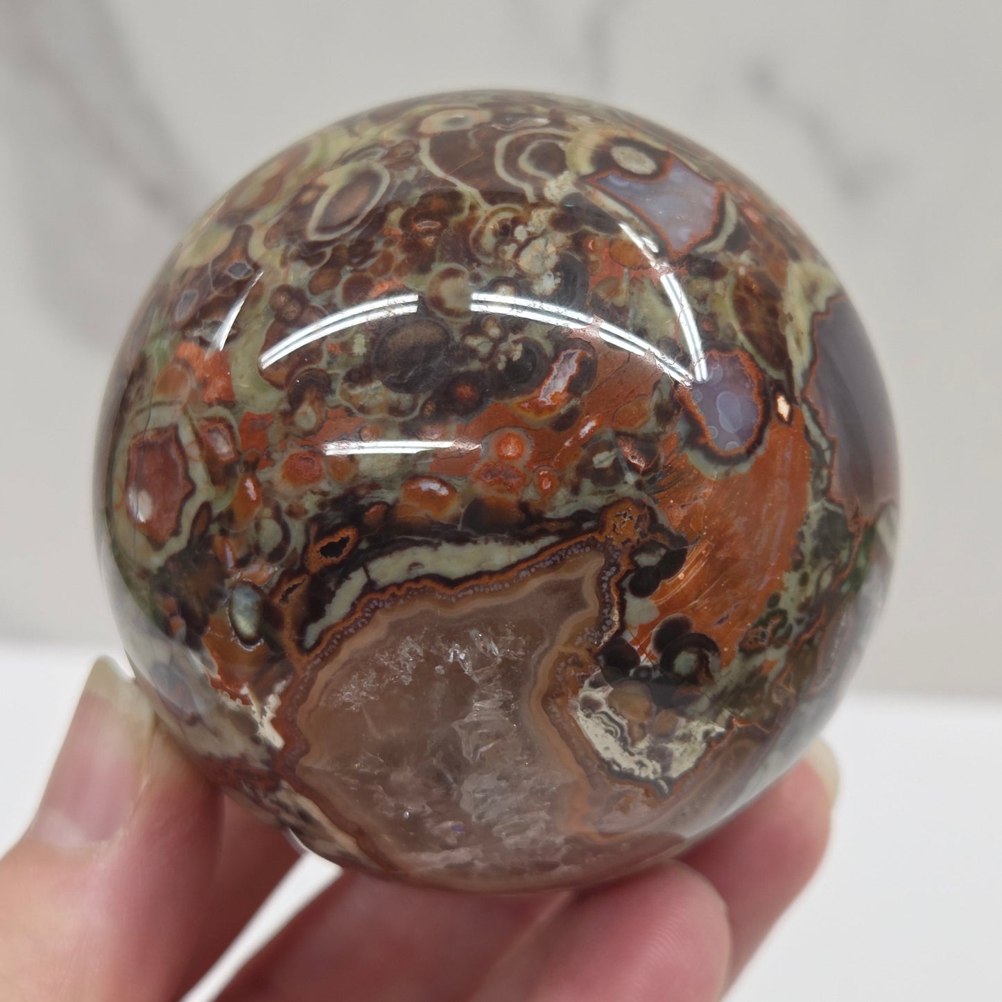 money agate multiple colored sphere held in a hand with a blurred background