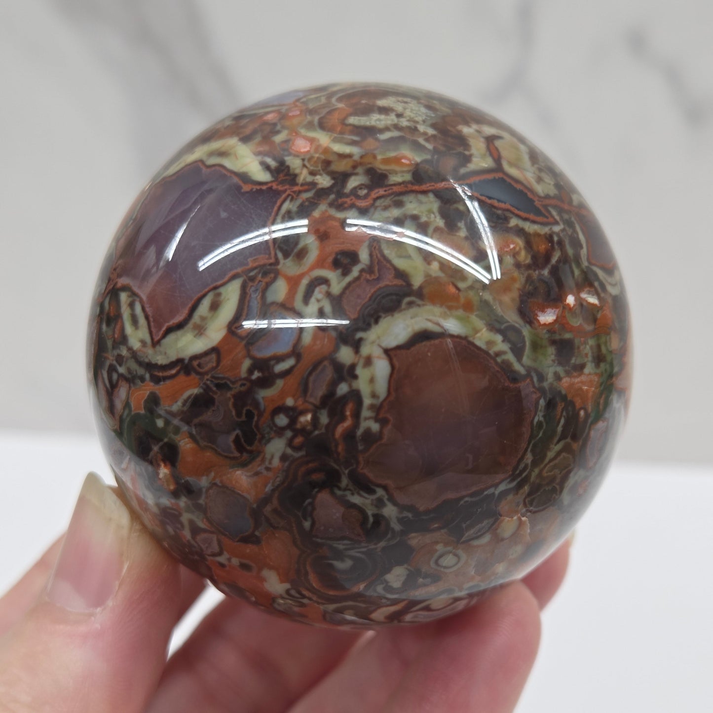 money agate multiple colored sphere held in a hand with a blurred background