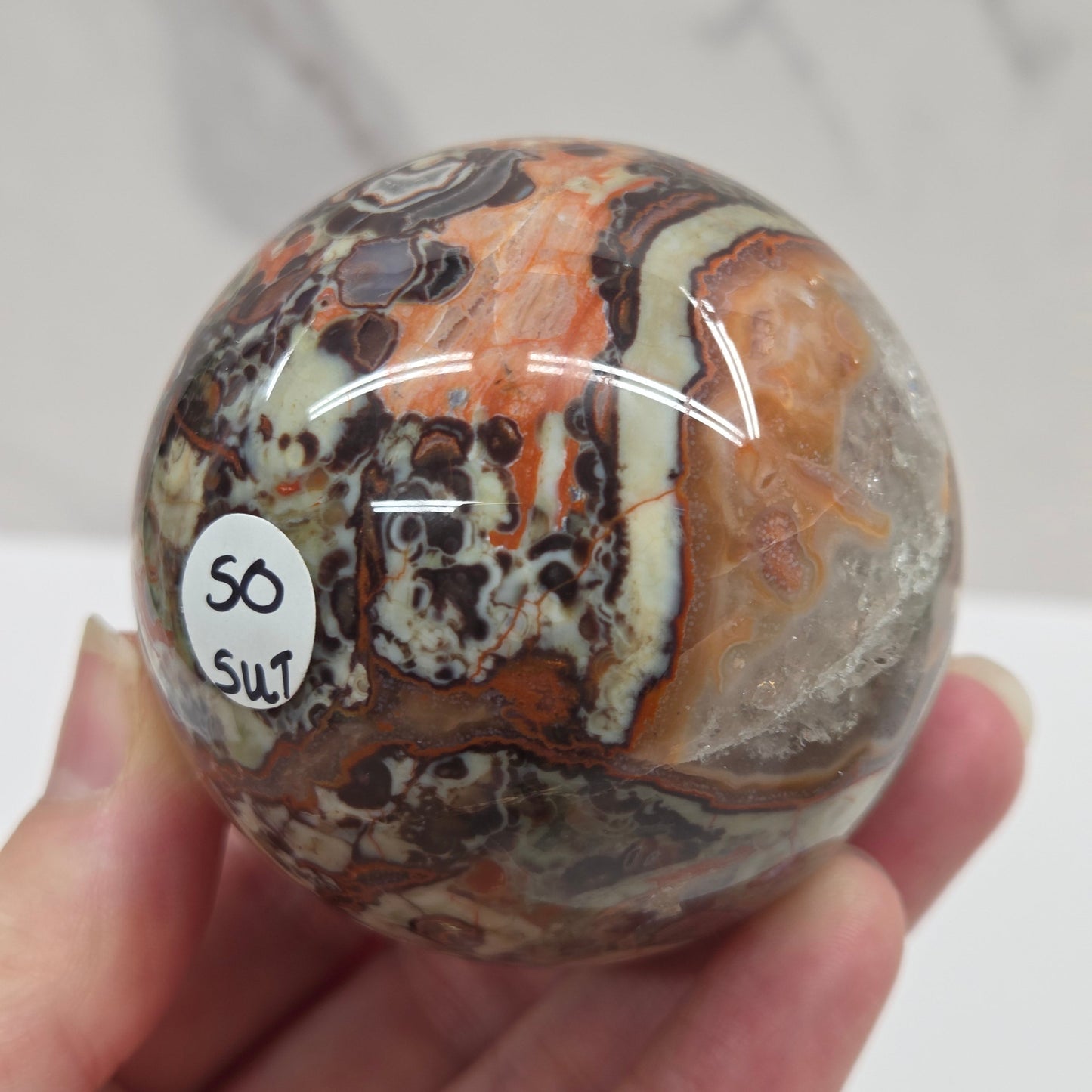 money agate multiple colored sphere held in a hand with a blurred background