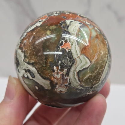 money agate multiple colored sphere held in a hand with a blurred background