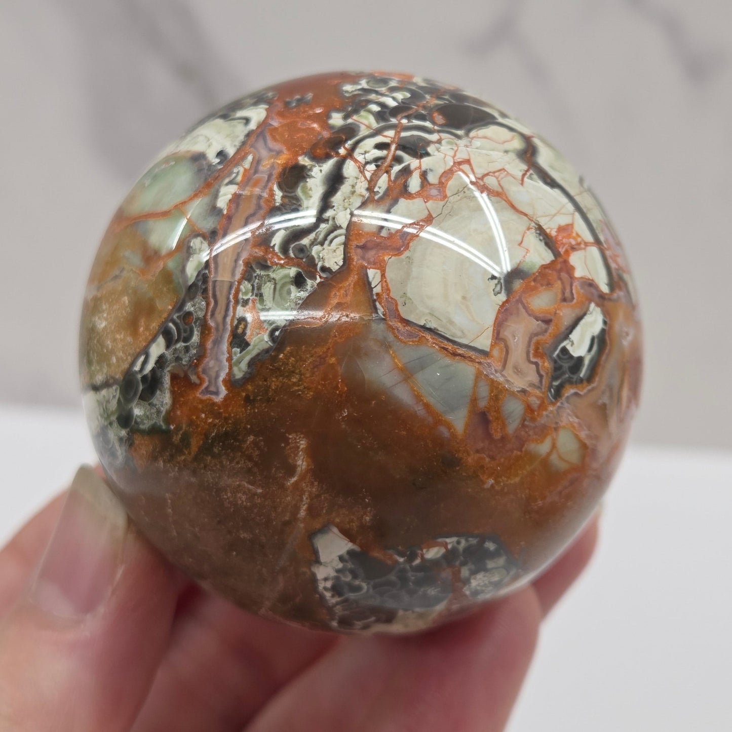 money agate multiple colored sphere held in a hand with a blurred background
