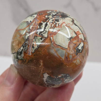 money agate multiple colored sphere held in a hand with a blurred background