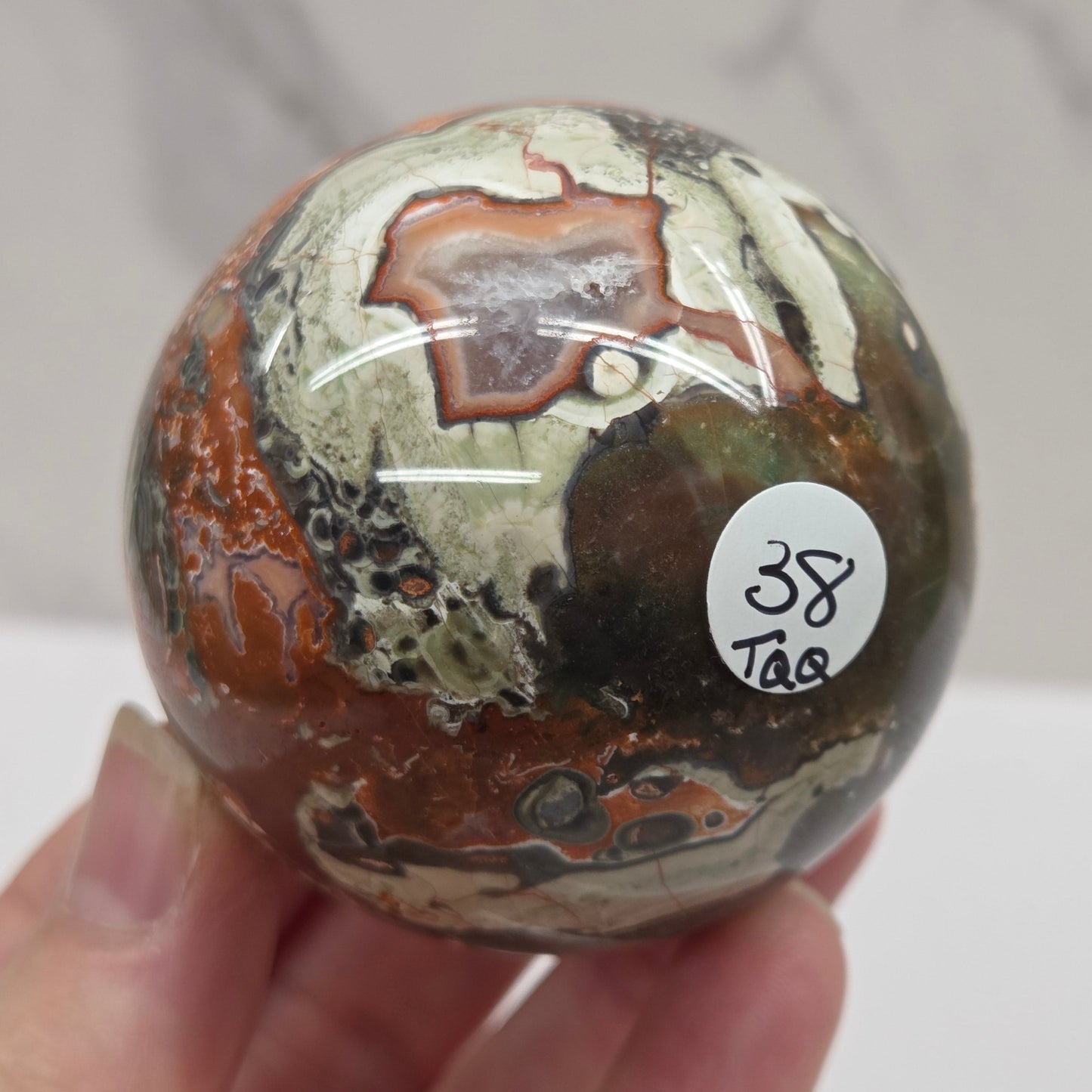 money agate multiple colored sphere held in a hand with a blurred background