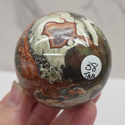 money agate multiple colored sphere held in a hand with a blurred background