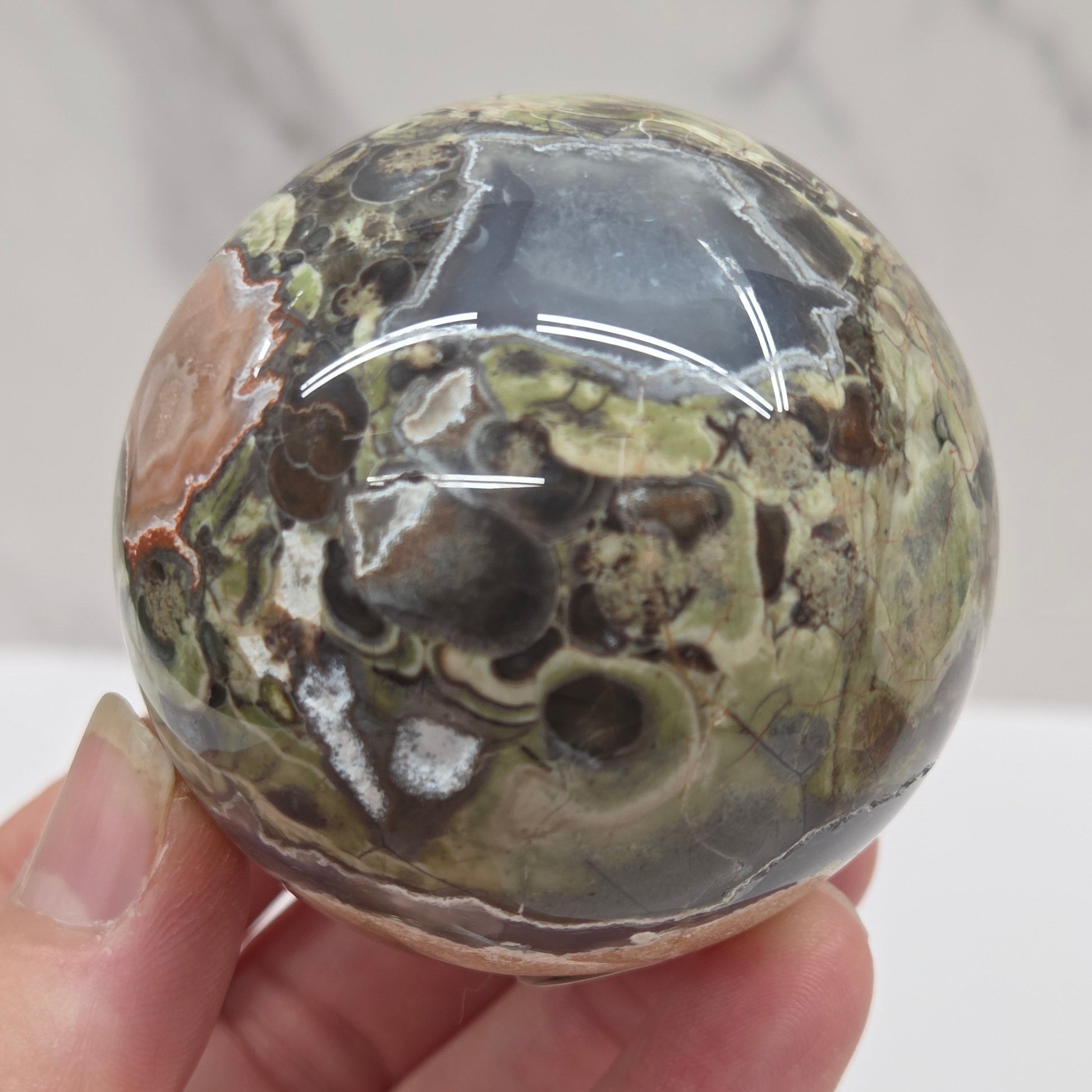money agate multiple colored sphere held in a hand with a blurred background
