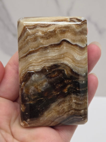 Hand holding a polished stone with brown and beige patterns against a neutral background