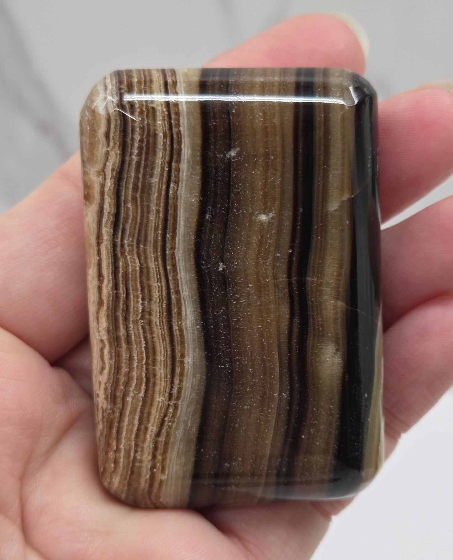Hand holding a rectangular chocolate calcite stone with striped pattern against a neutral background