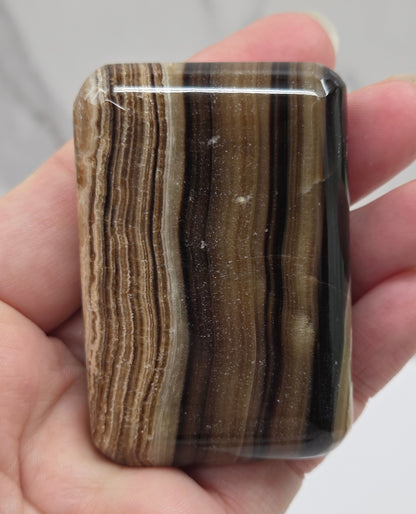 Hand holding a rectangular chocolate calcite stone with striped pattern against a neutral background
