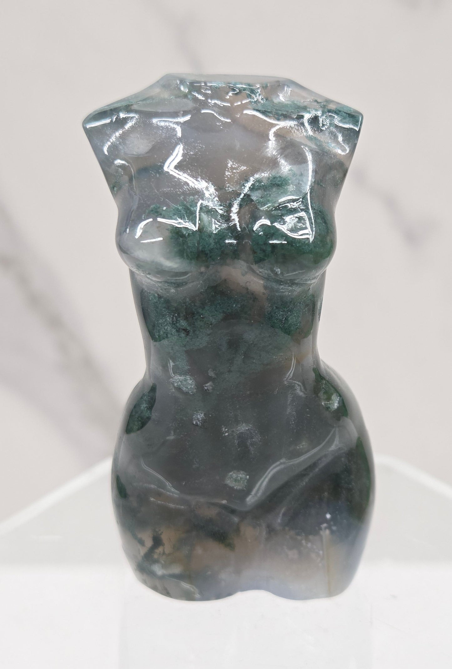 Moss agate carving of abstract human figures on a white surface with a marble-patterned wall in the background.