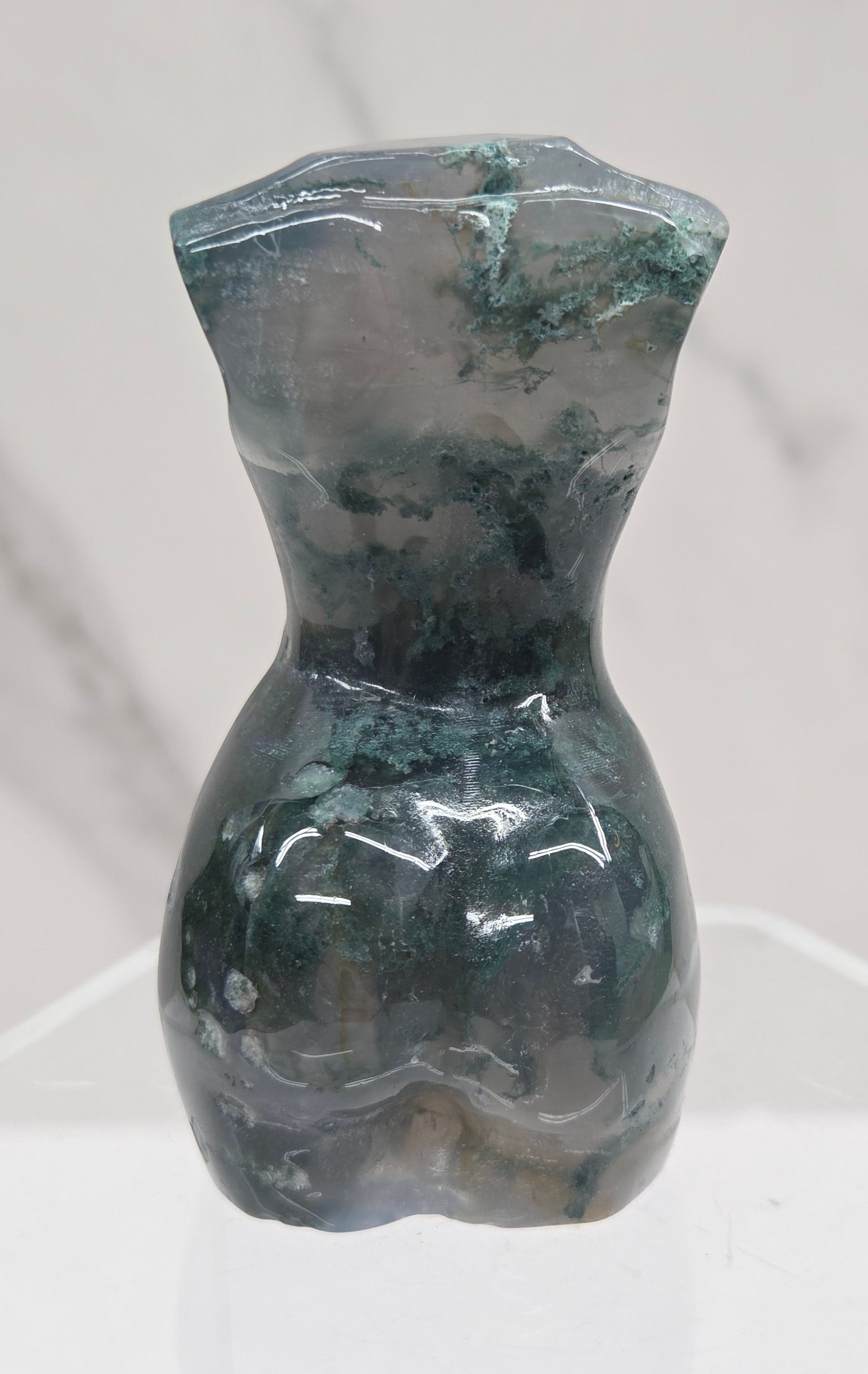 Moss agate carving of abstract human figures on a white surface with a marble-patterned wall in the background.