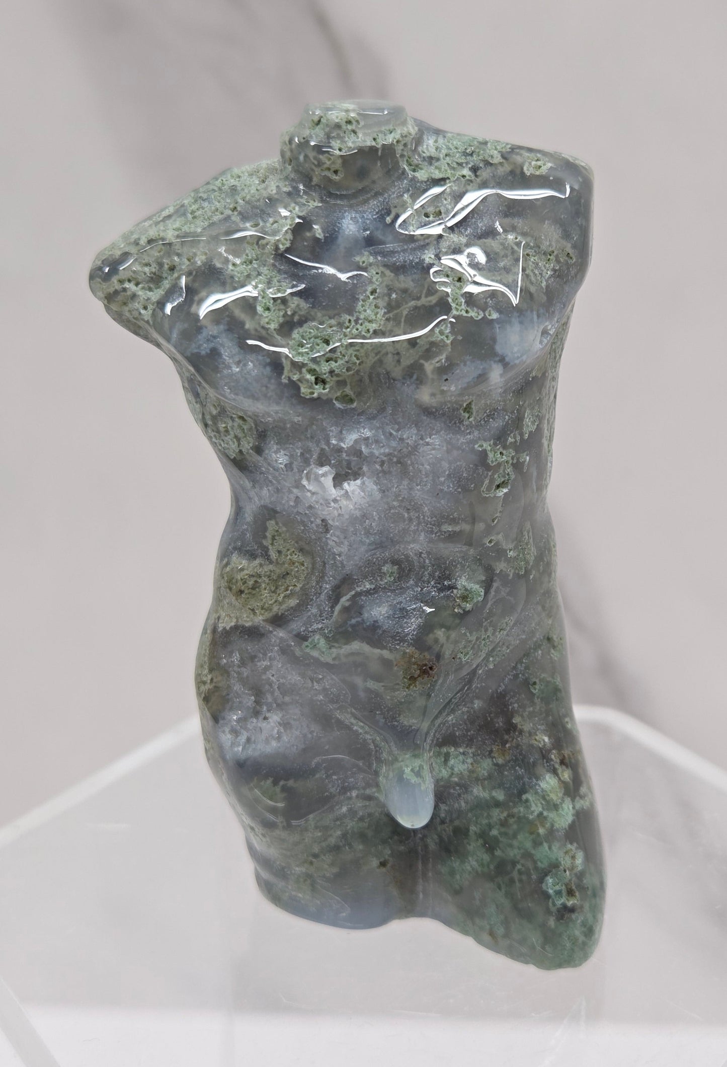 Moss agate carving of abstract human figures on a white surface with a marble-patterned wall in the background.