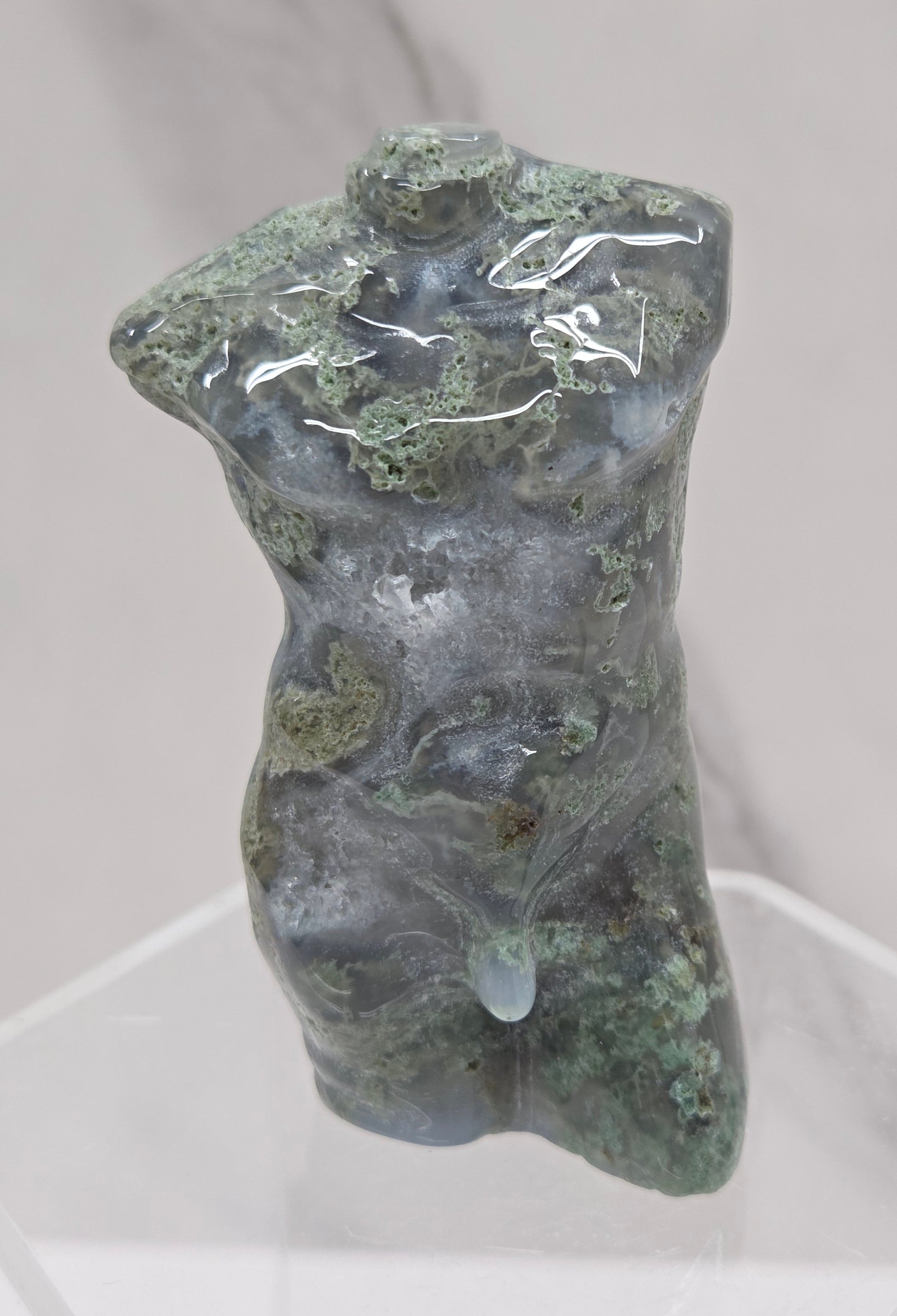 Moss agate carving of abstract human figures on a white surface with a marble-patterned wall in the background.