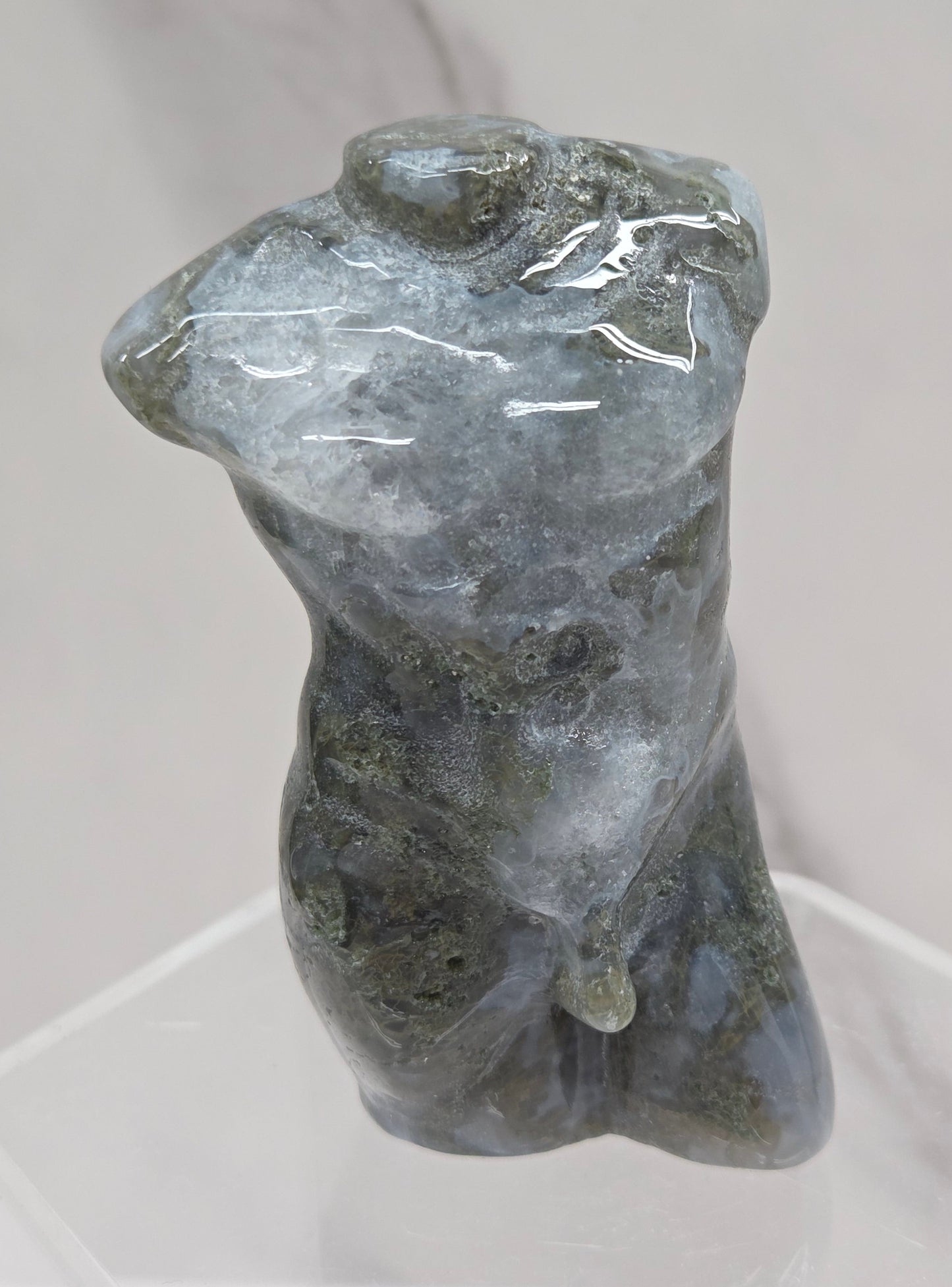 Moss agate carving of abstract human figures on a white surface with a marble-patterned wall in the background.