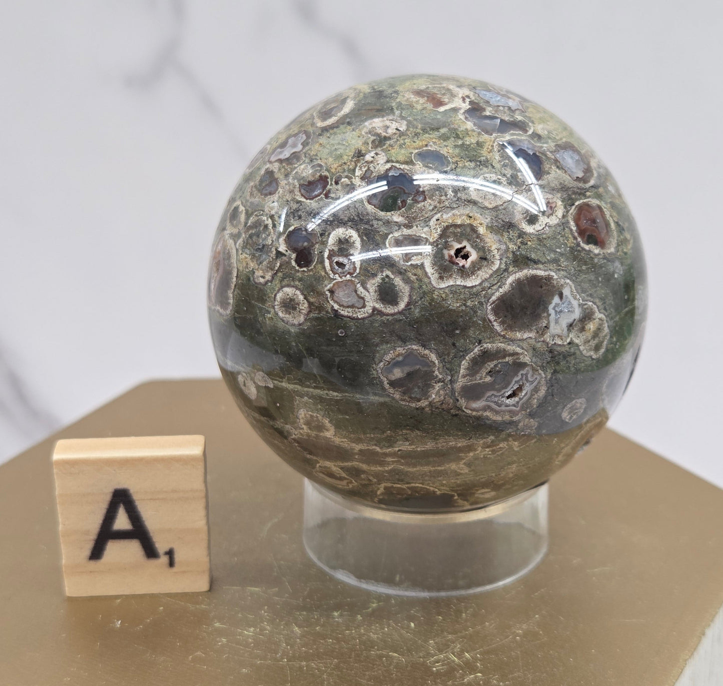 Rainforest Jasper sphere with orbicular designs on a wood stand with a white background