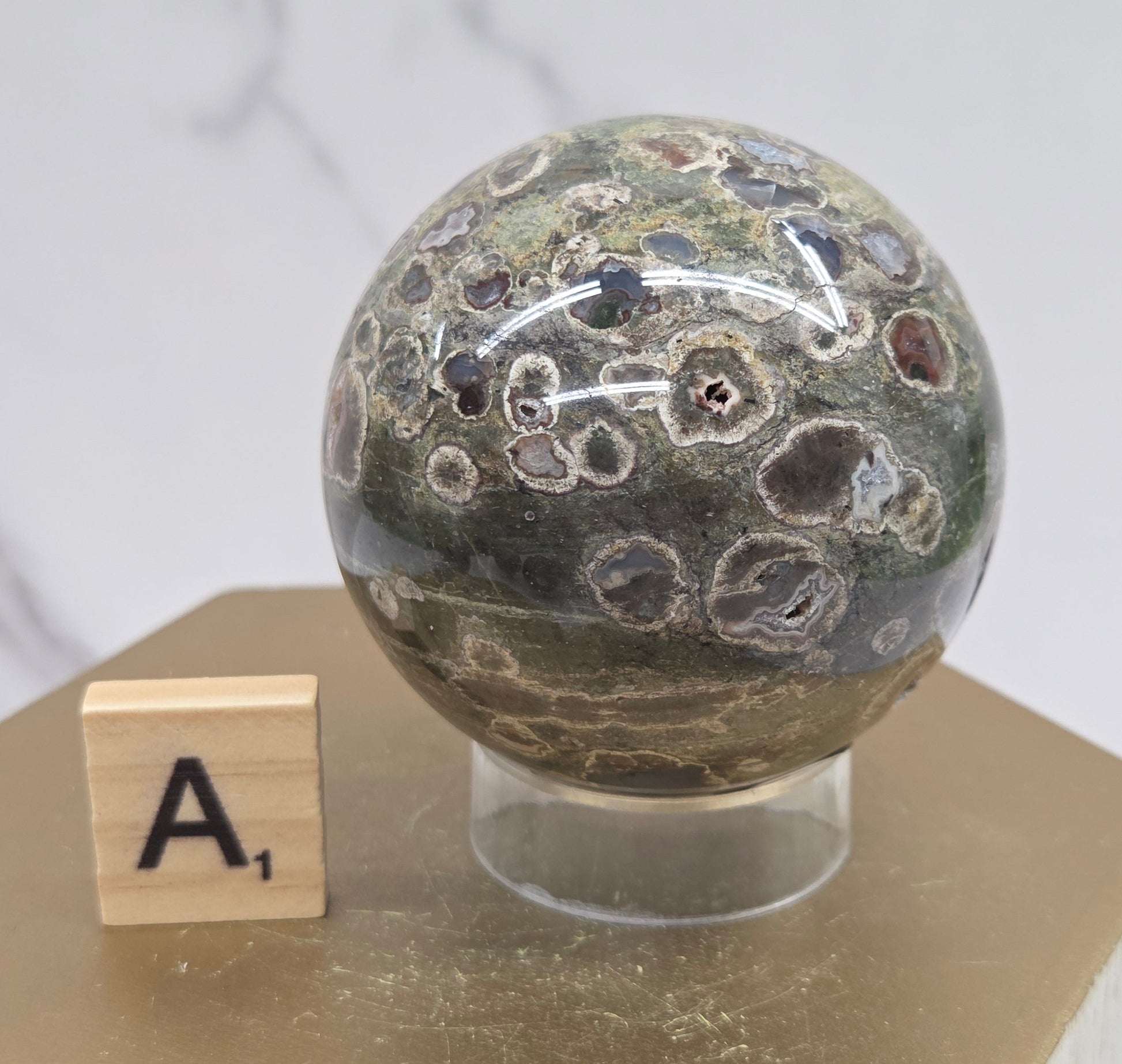 Rainforest Jasper sphere with orbicular designs on a wood stand with a white background