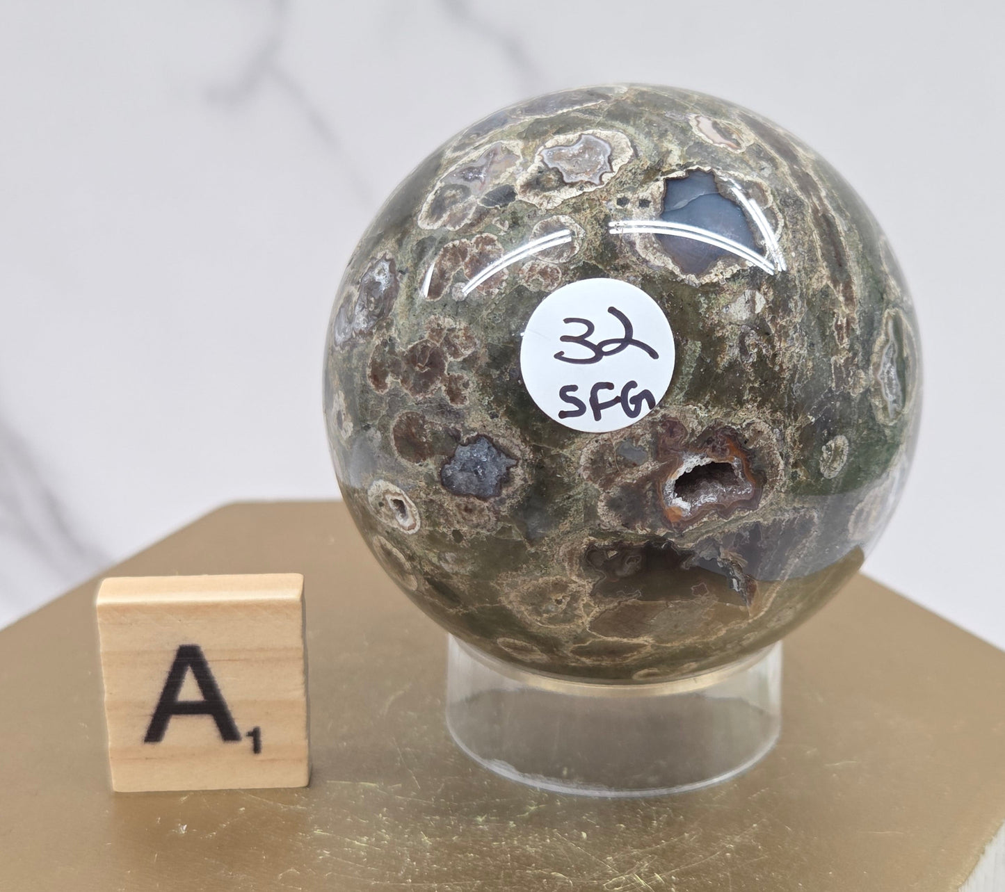 Rainforest Jasper sphere with orbicular designs on a wood stand with a white background
