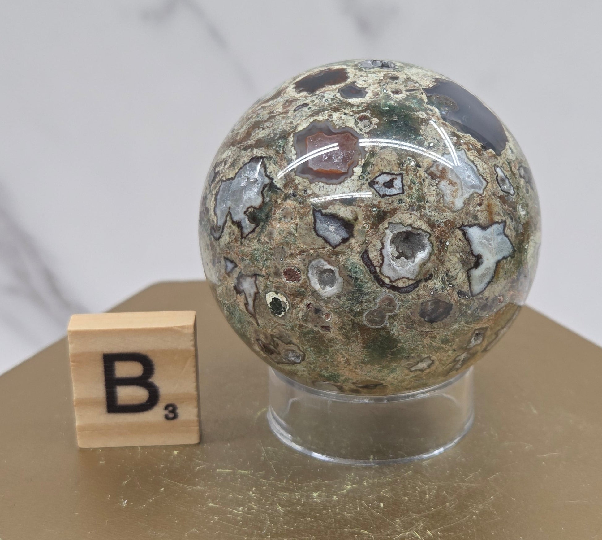 Rainforest Jasper sphere with orbicular designs on a wood stand with a white background