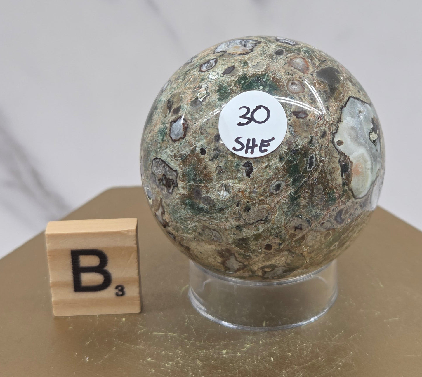 Rainforest Jasper sphere with orbicular designs on a wood stand with a white background