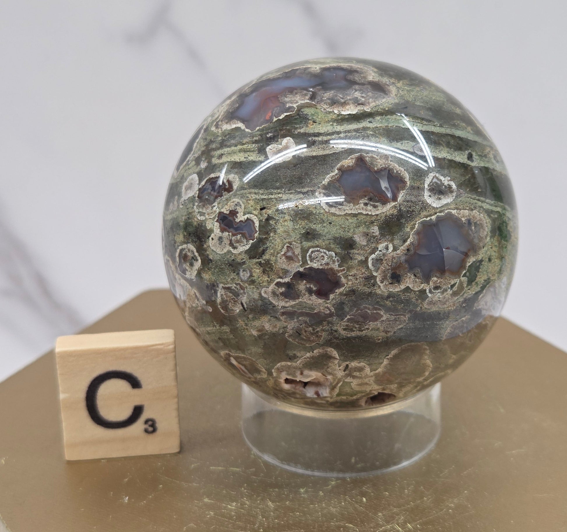 Rainforest Jasper sphere with orbicular designs on a wood stand with a white background