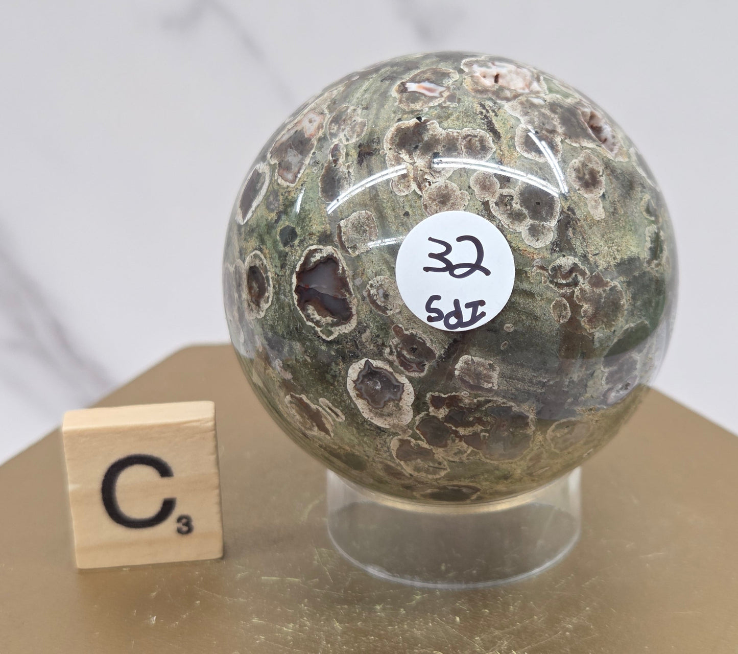 Rainforest Jasper sphere with orbicular designs on a wood stand with a white background