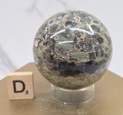 Rainforest Jasper sphere with orbicular designs on a wood stand with a white background