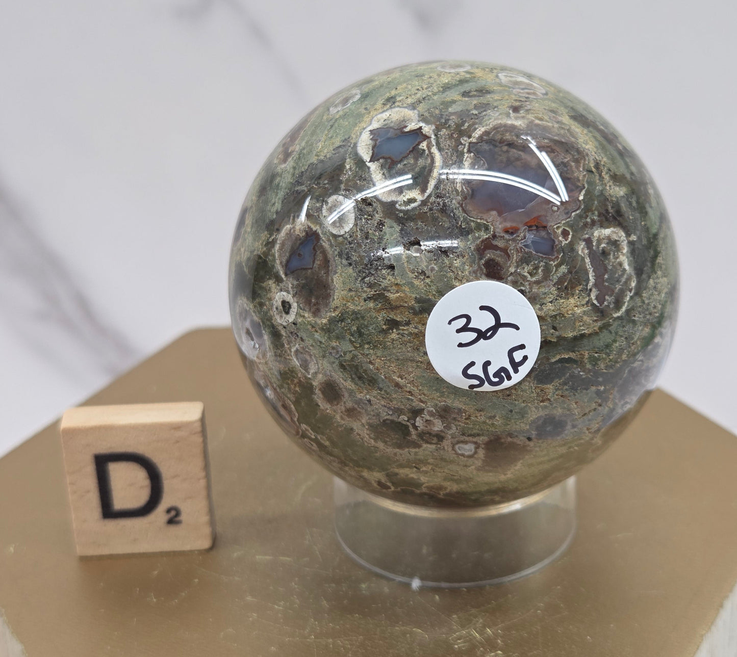 Rainforest Jasper sphere with orbicular designs on a wood stand with a white background