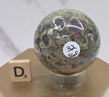 Rainforest Jasper sphere with orbicular designs on a wood stand with a white background