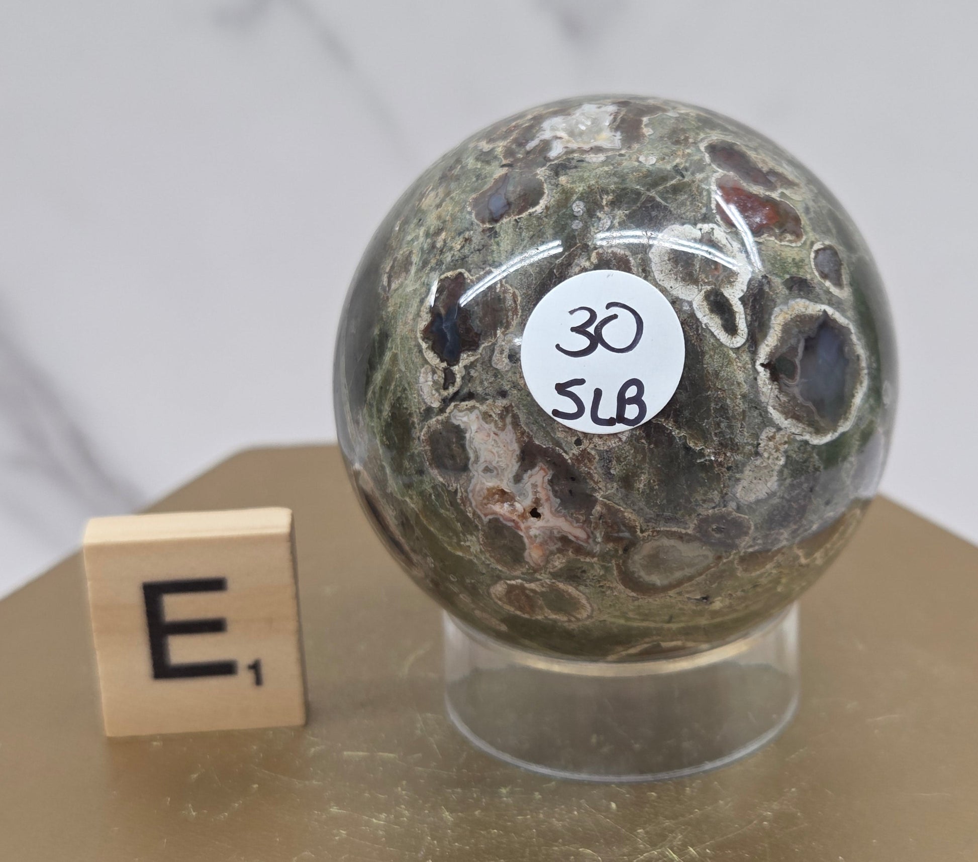 Rainforest Jasper sphere with orbicular designs on a wood stand with a white background