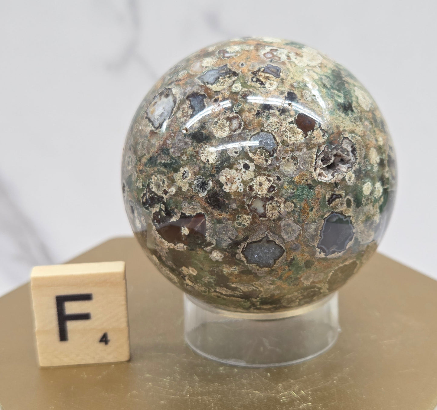 Rainforest Jasper sphere with orbicular designs on a wood stand with a white background