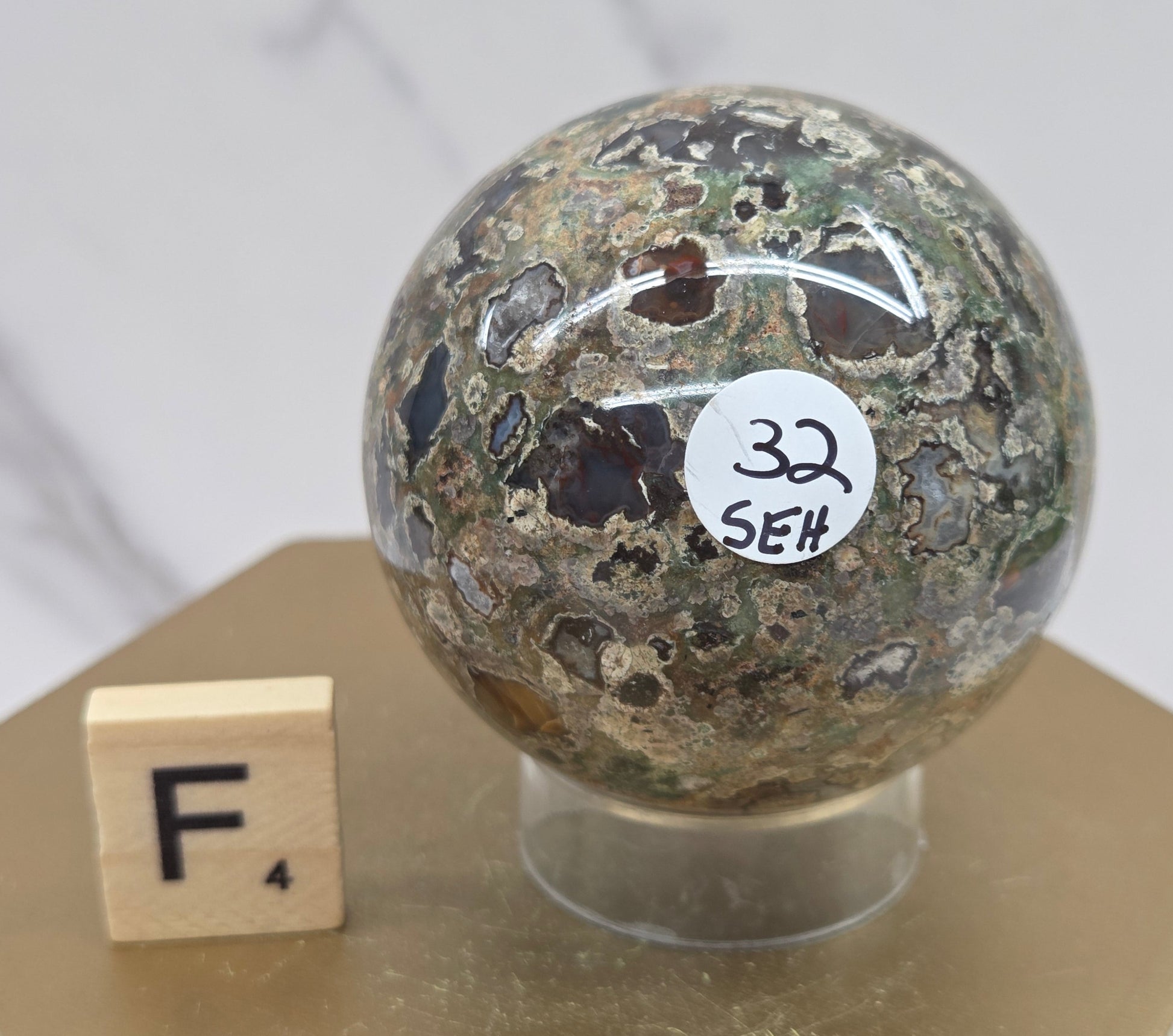 Rainforest Jasper sphere with orbicular designs on a wood stand with a white background