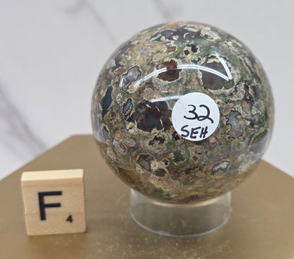 Rainforest Jasper sphere with orbicular designs on a wood stand with a white background