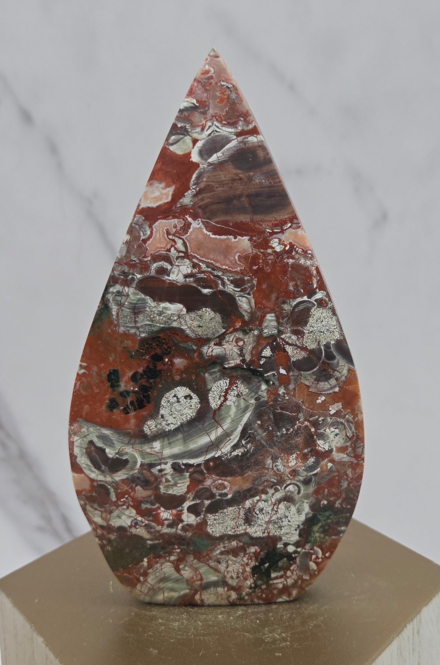 money agate multiple colored teardrop shaped carving on a wooden stand with a blurred background