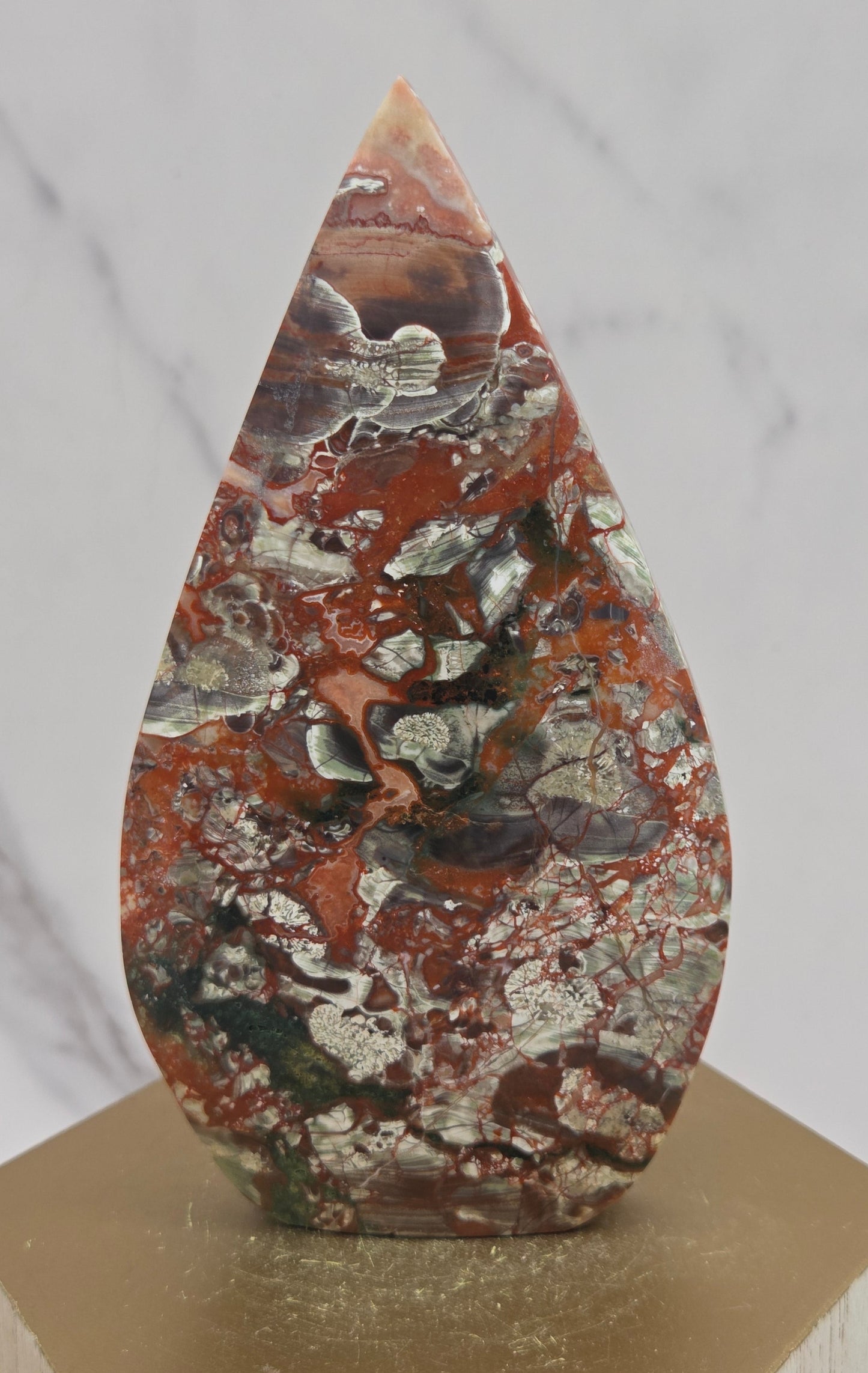 money agate multiple colored teardrop shaped carving on a wooden stand with a blurred background