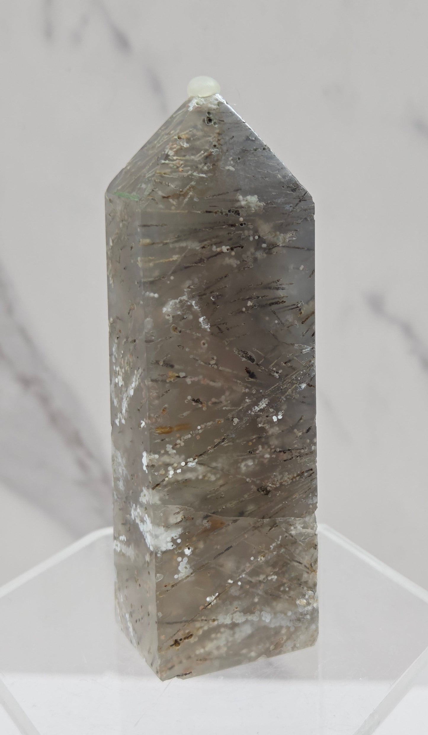 Crystal point with inclusions on a clear stand against a white background