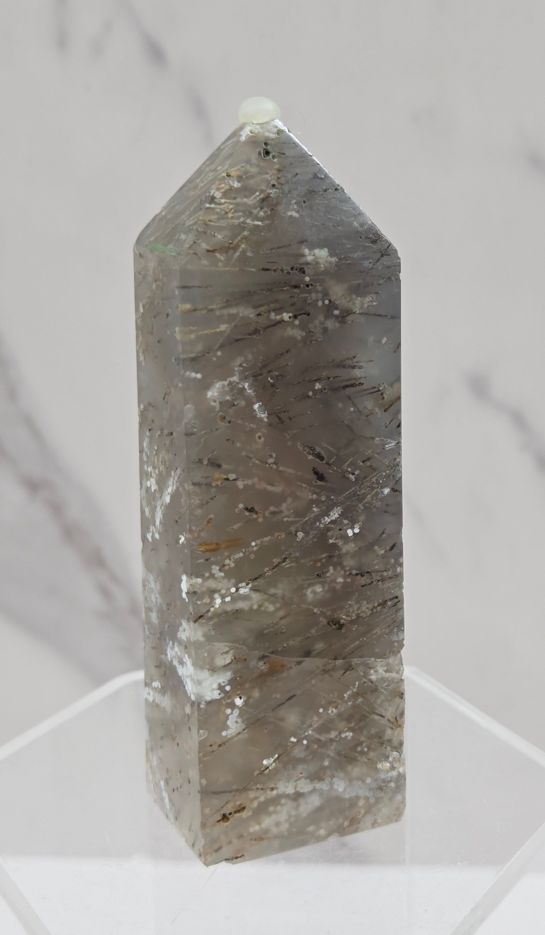 Crystal point with inclusions on a clear stand against a white background