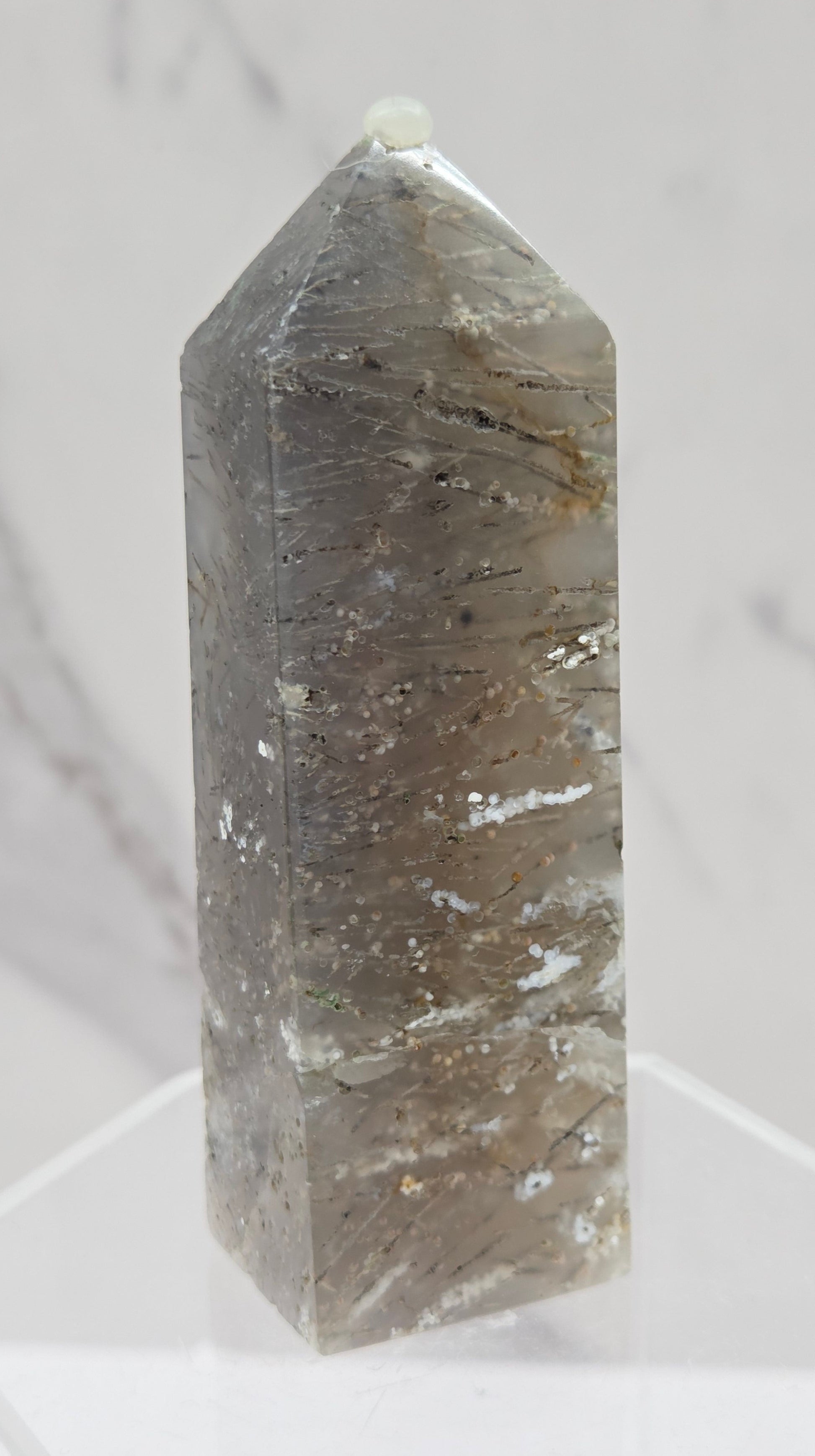Crystal point with inclusions on a clear stand against a white background