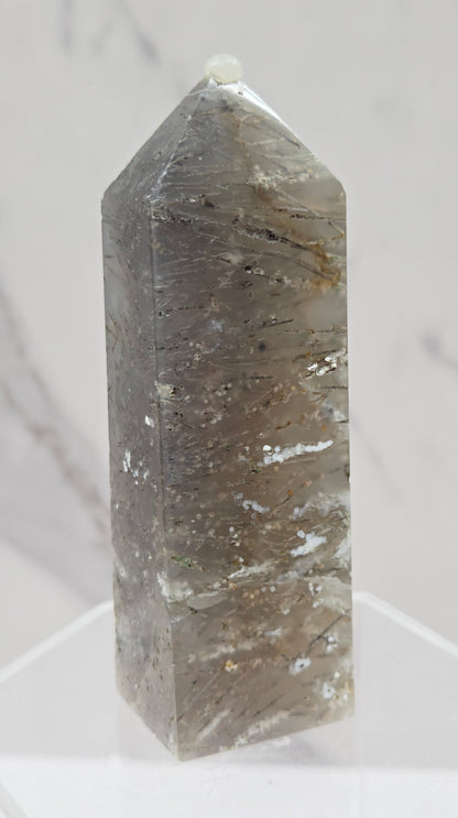 Crystal point with inclusions on a clear stand against a white background
