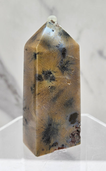 Crystal point with inclusions on a clear stand against a white background