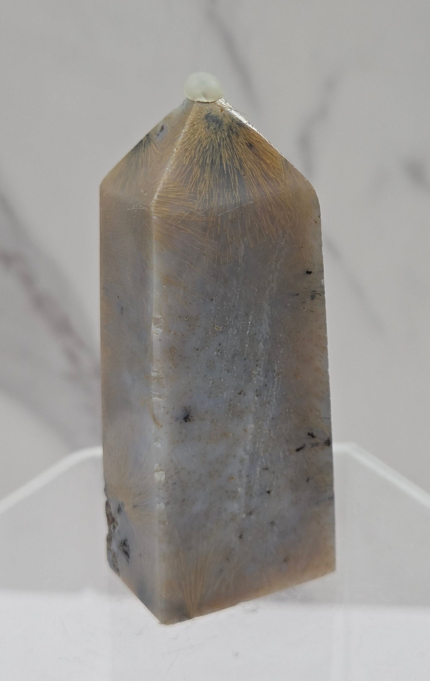 Crystal point with inclusions on a clear stand against a white background