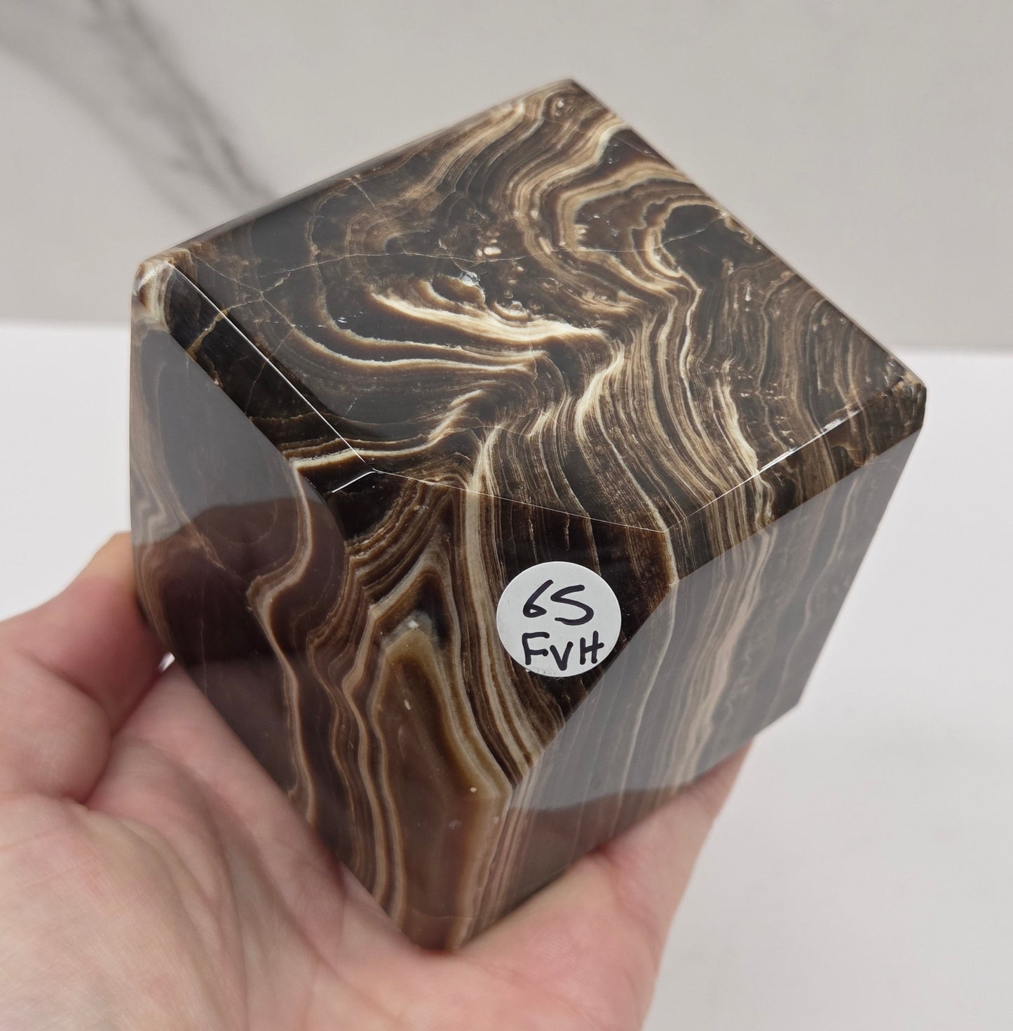 Hand holding a marbled chocolate calcite cube on a white background