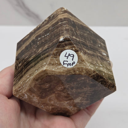 Hand holding a marbled chocolate calcite cube on a white background