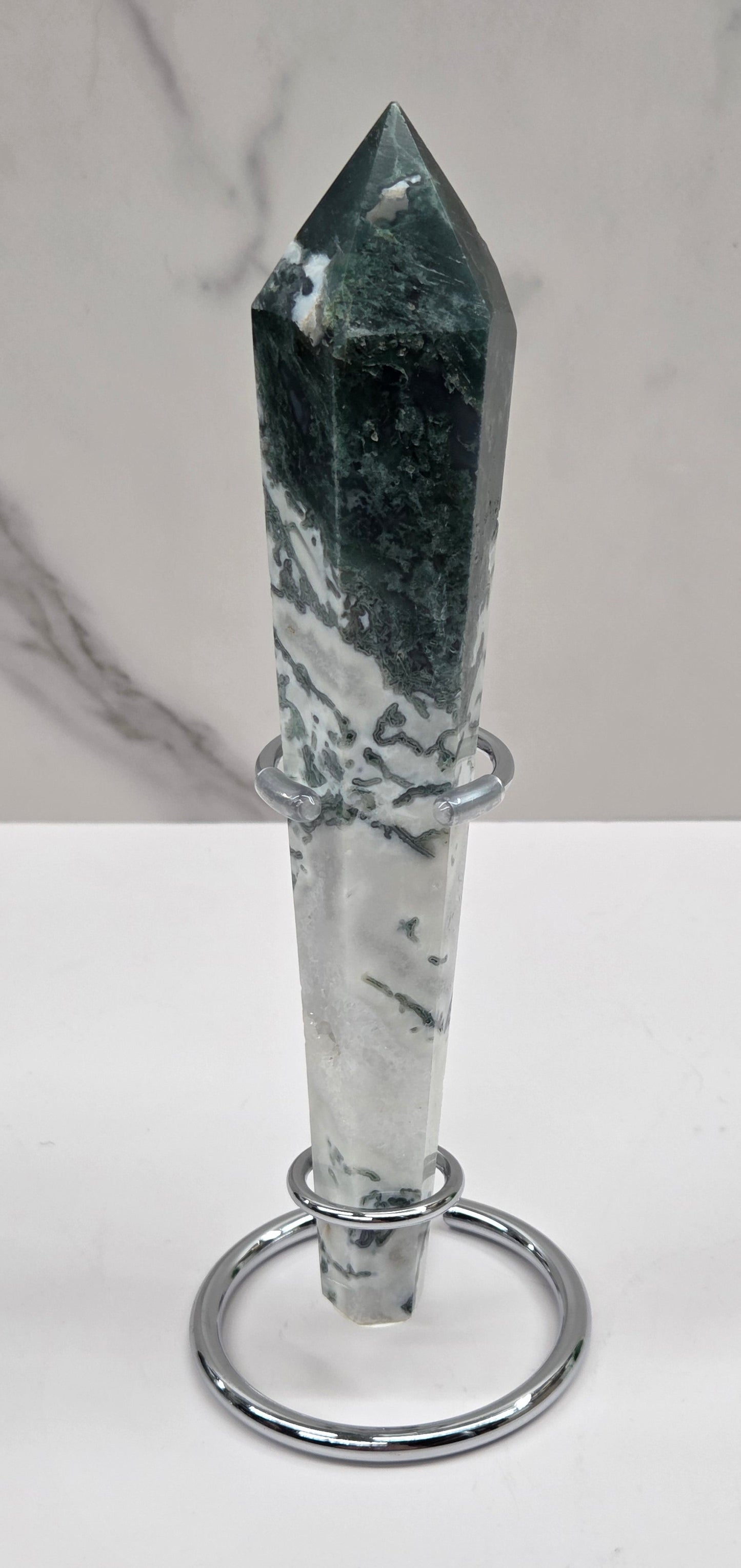 Moss agate wand carving in a silver stand against a white background