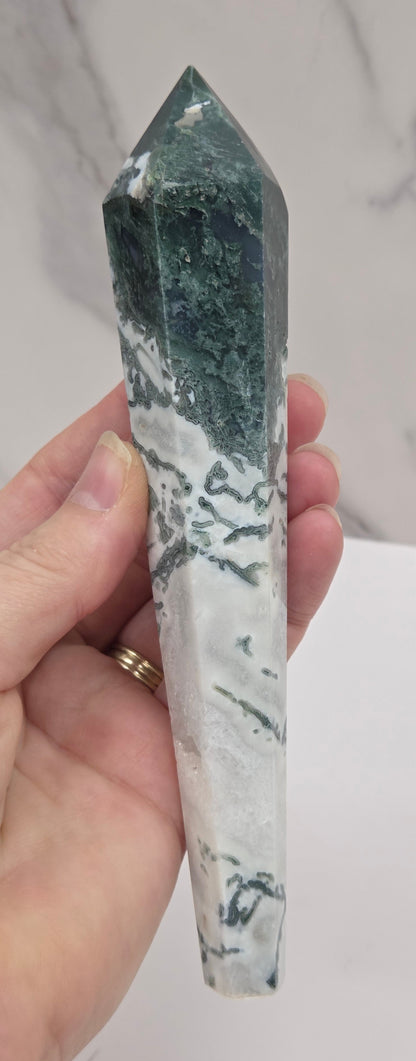 Hand holding a moss agate wand carving against a white background