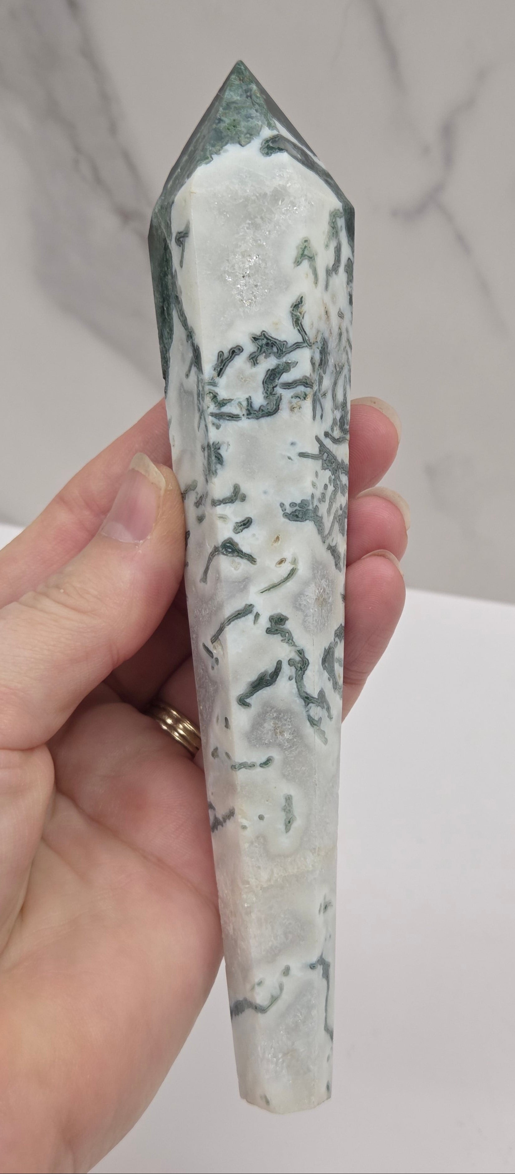 Hand holding a moss agate wand carving against a white background