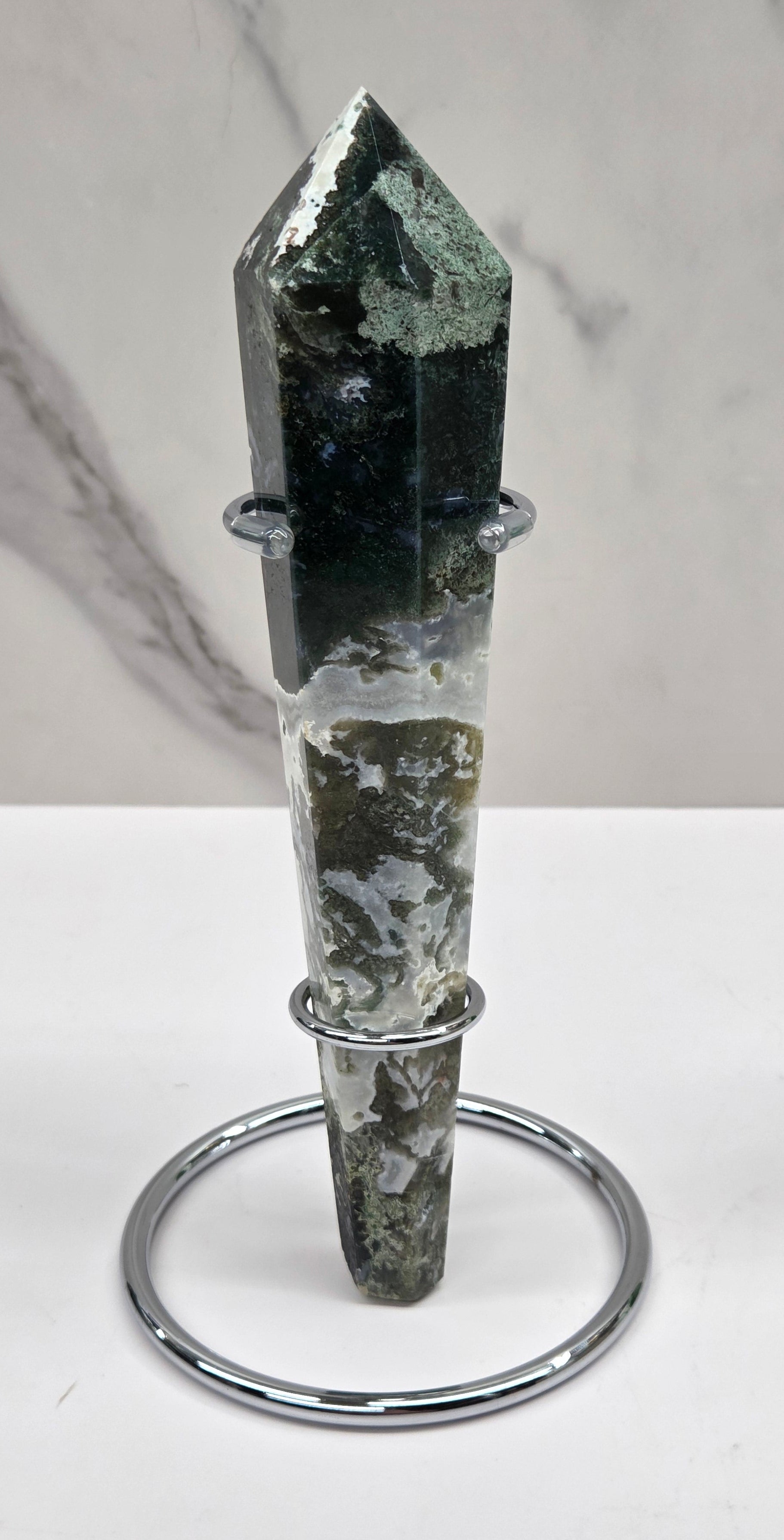 Moss agate wand carving in a silver stand against a white background