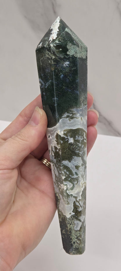 Hand holding a moss agate wand carving against a white background