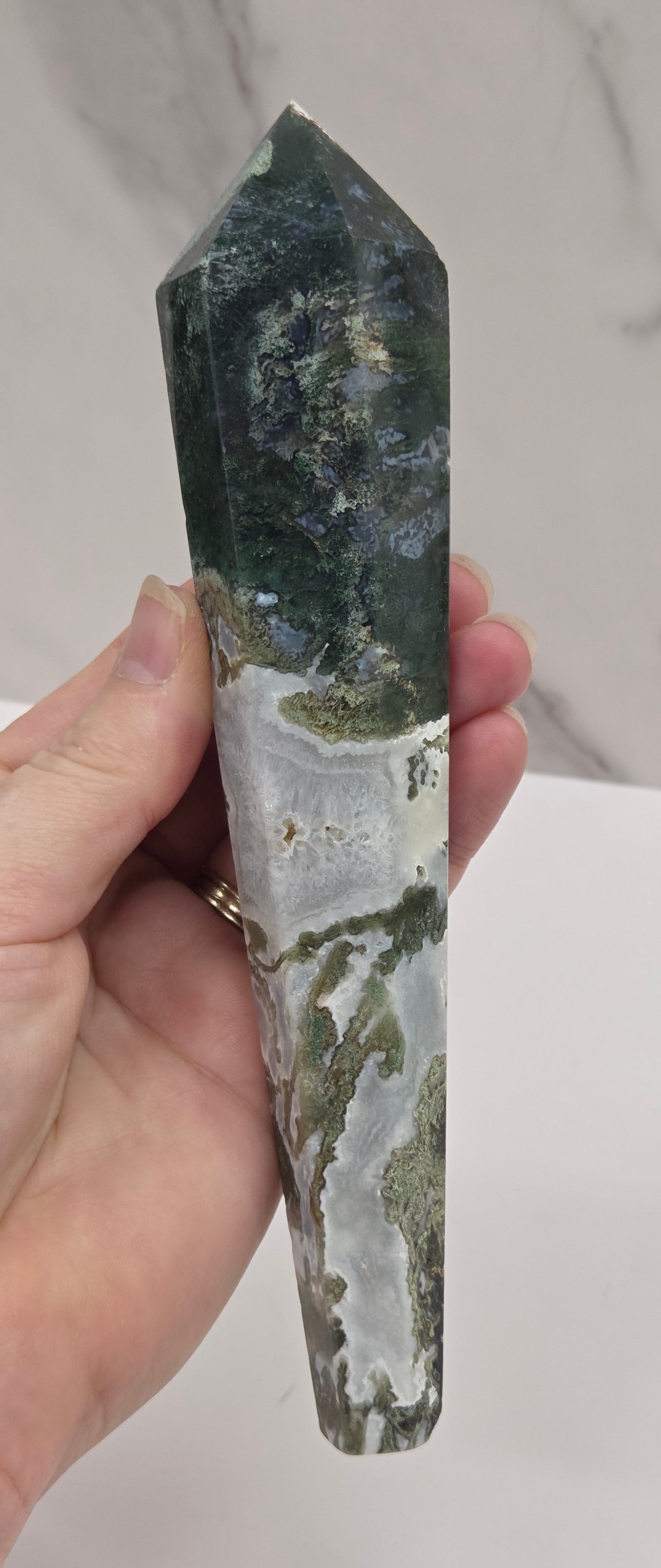 Hand holding a moss agate wand carving against a white background