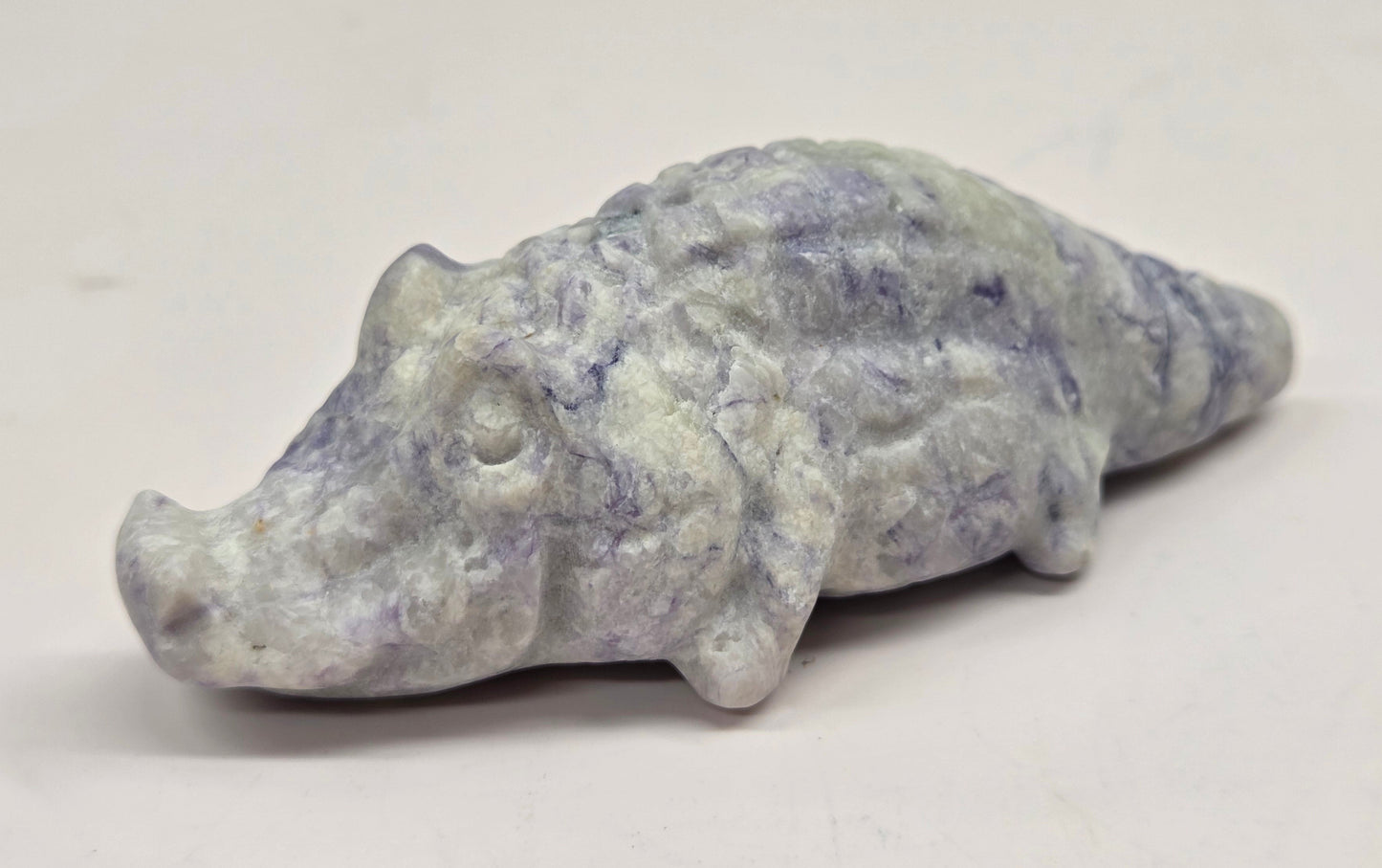 Carved lavender jasper crocodile on a white background